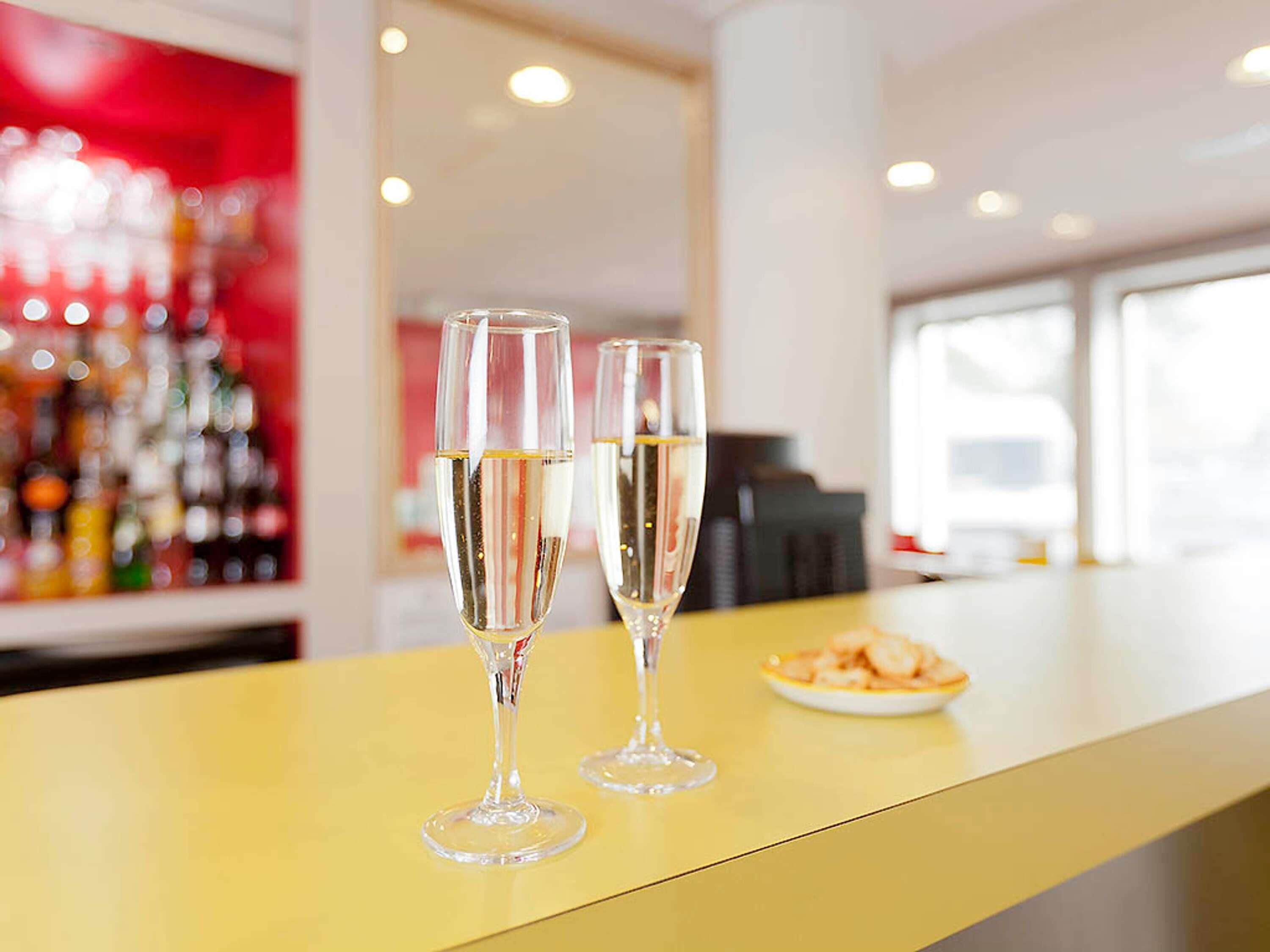 Two champagne flutes on a yellow bar counter with a plate of shrimp and a red-lit background.
