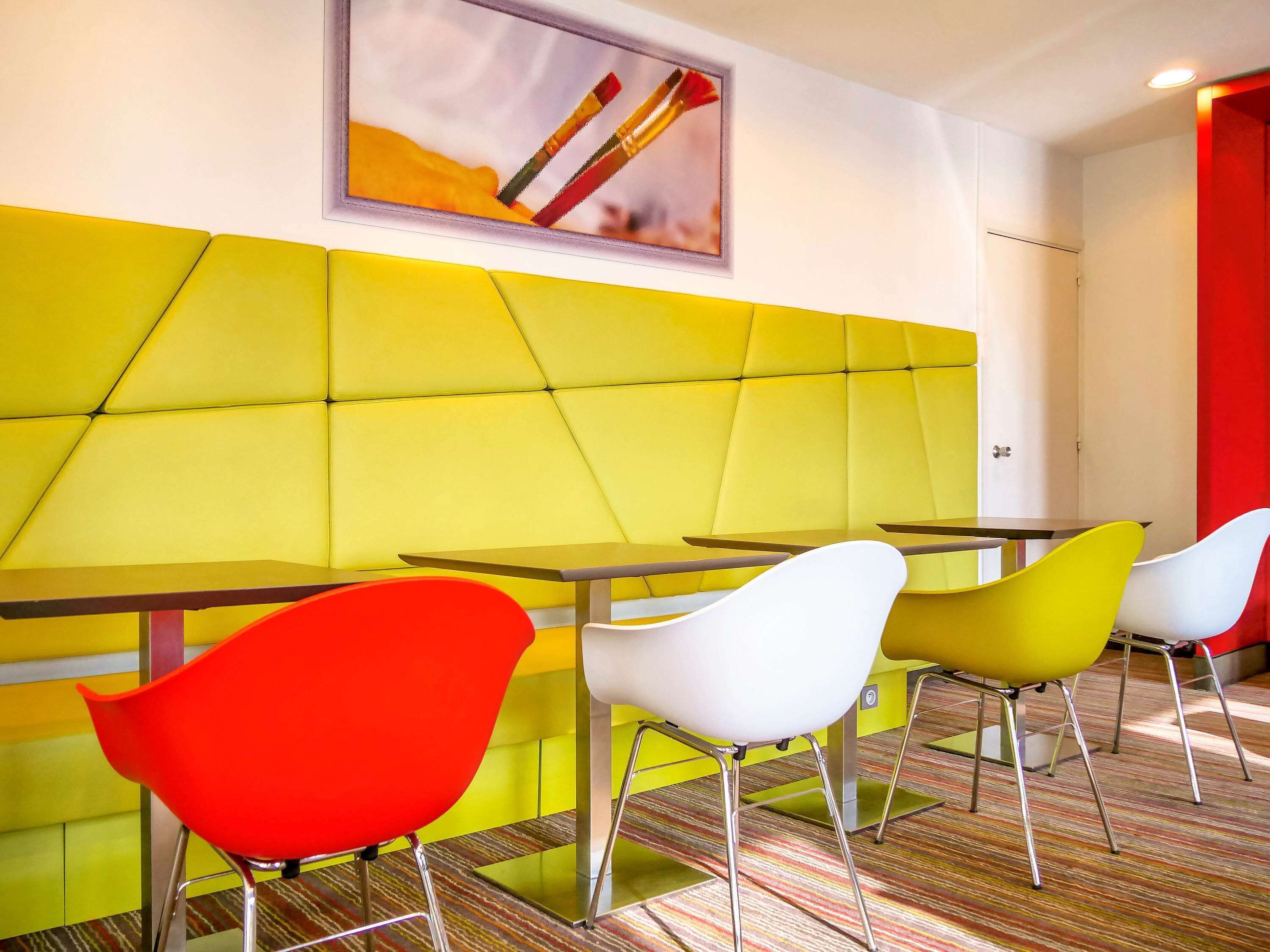 Un área de comedor moderna con asientos de color amarillo y rojo vibrantes, piso a rayas y un cuadro enmarcado en la pared.