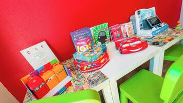 A table with educational toys and books, green chairs, and a red wall.