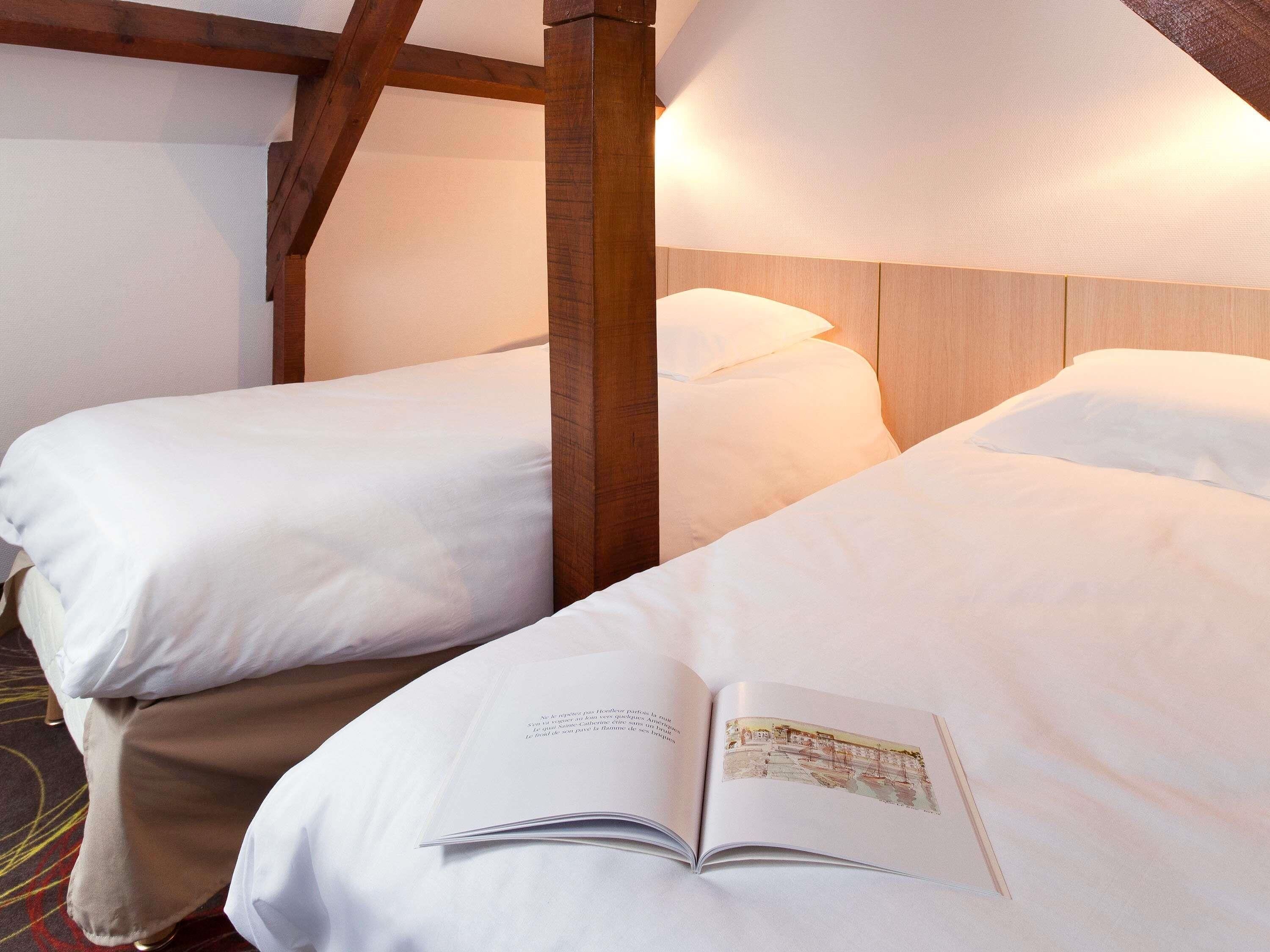 A hotel room with two beds, wooden headboard, and a book on the bed.