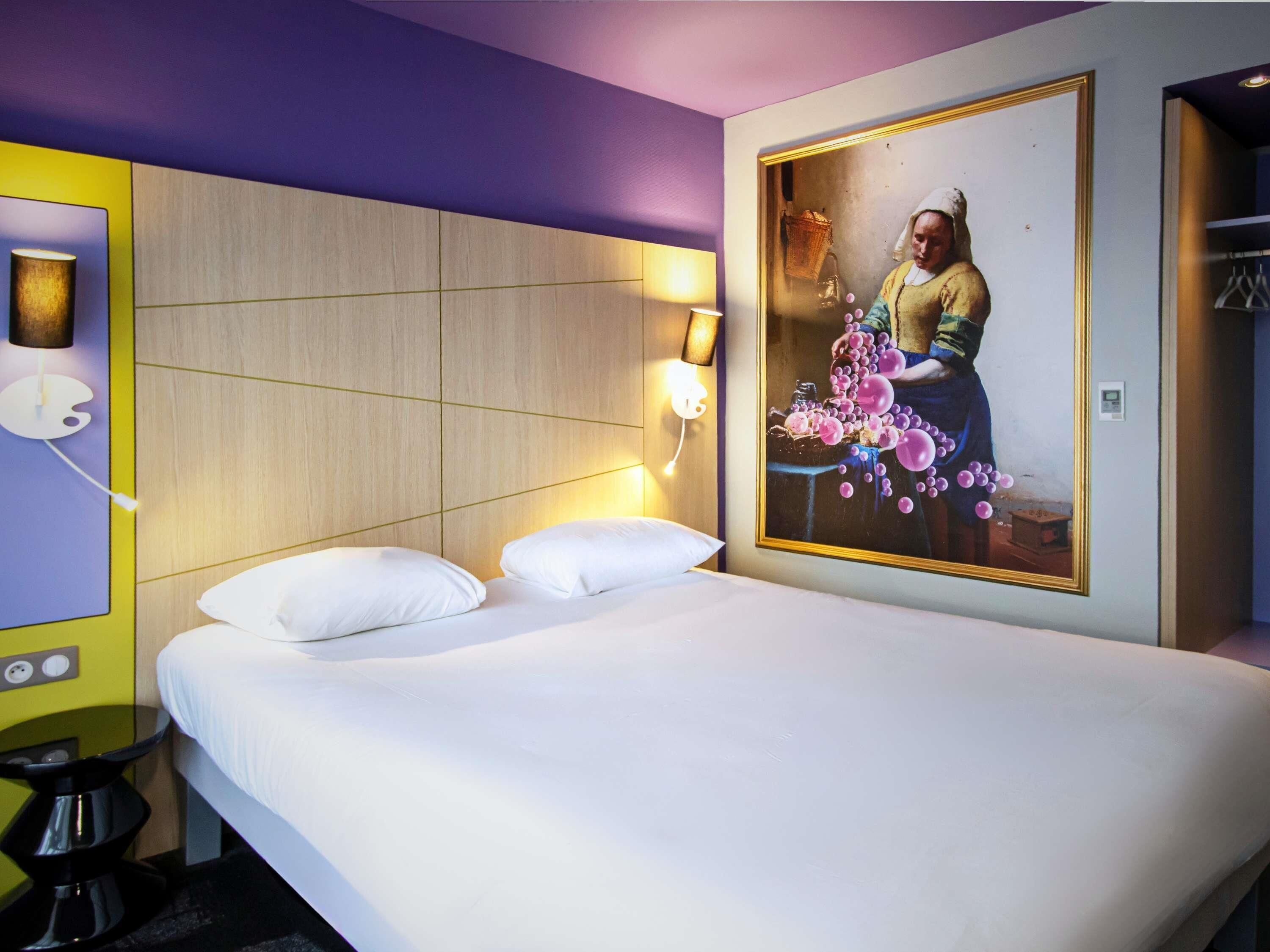 Una habitación de hotel con cama, un cuadro colgado en la pared y un armario.