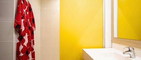 A bathroom with a white sink, yellow accent wall, and a red floral shower curtain.