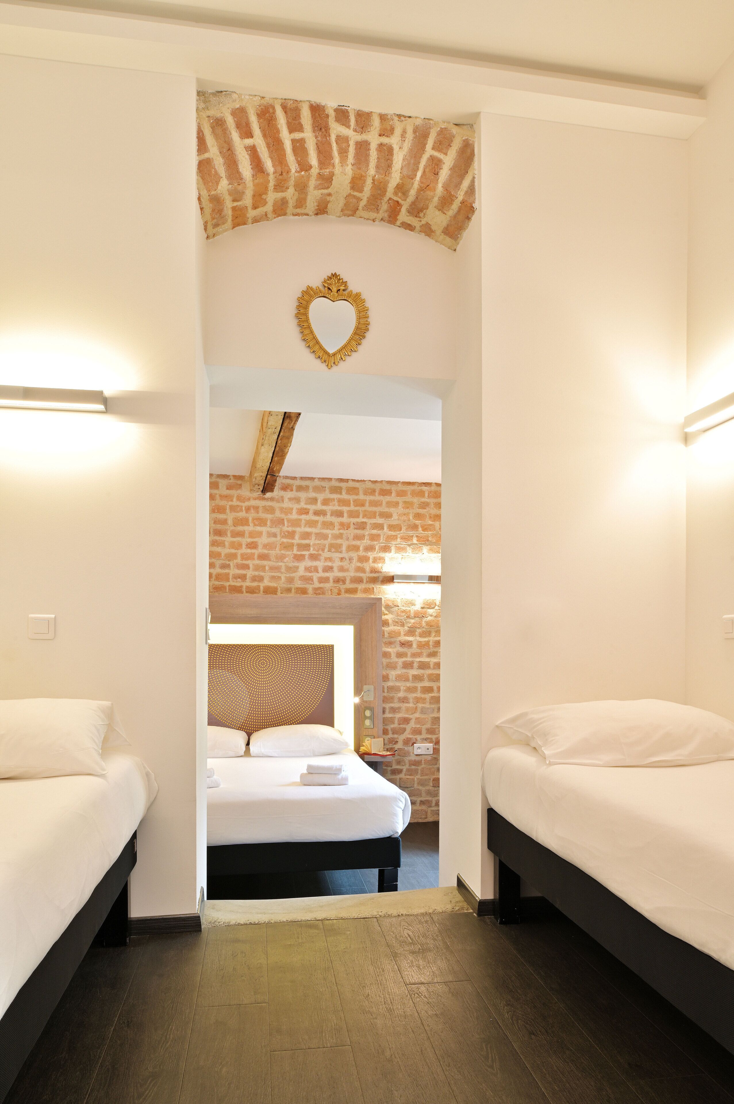 Une chambre d’hôtel avec deux lits, un mur en briques, une décoration en forme de cœur et une lucarne.
