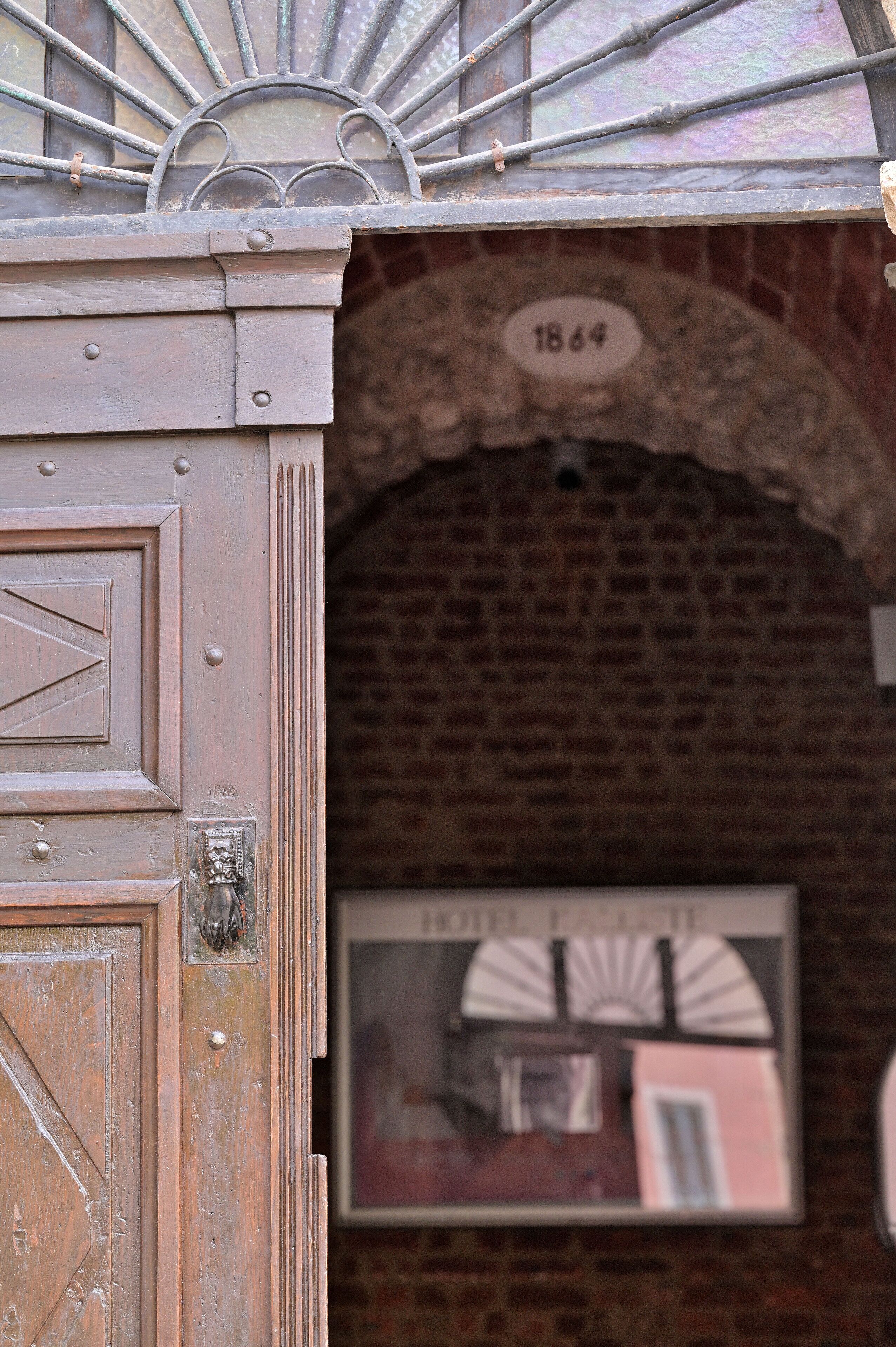 Una antigua puerta de madera con una reja metálica, un muro de ladrillo y una placa con la fecha 1864.