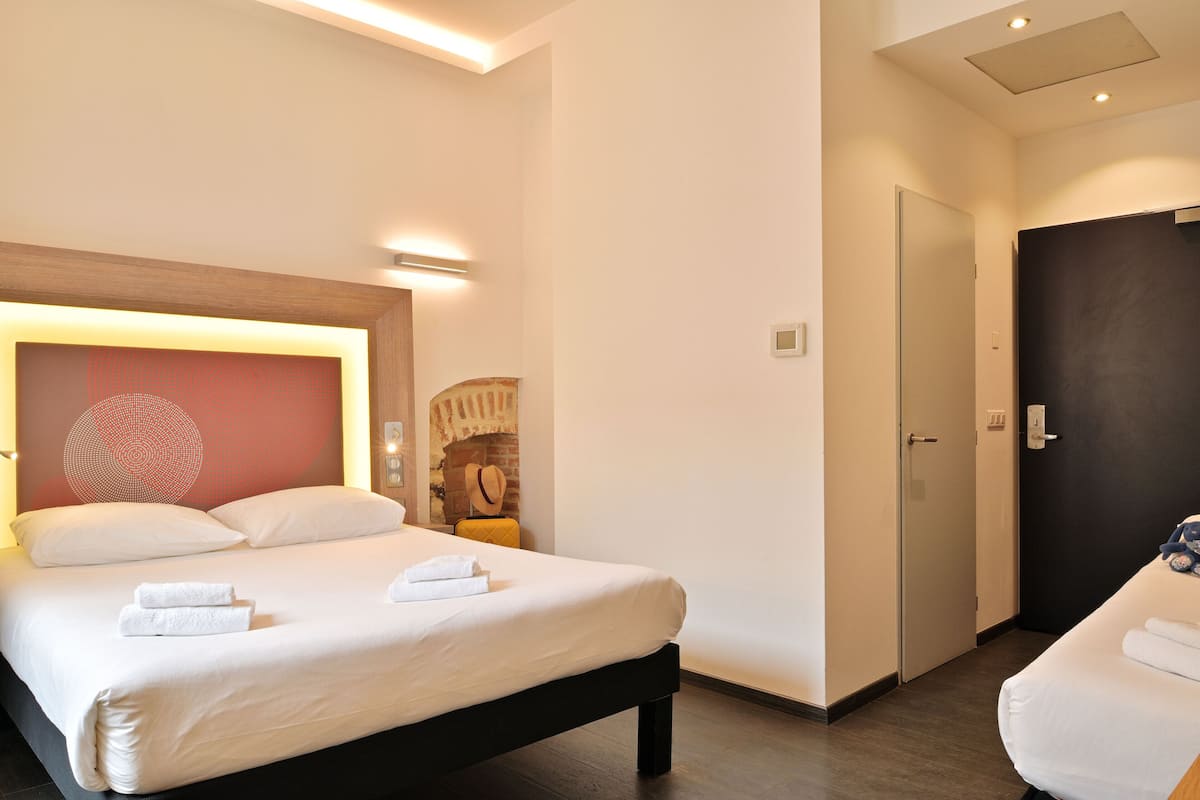 A hotel room with a large bed, a bedside table, a chair, and a wall-mounted TV.