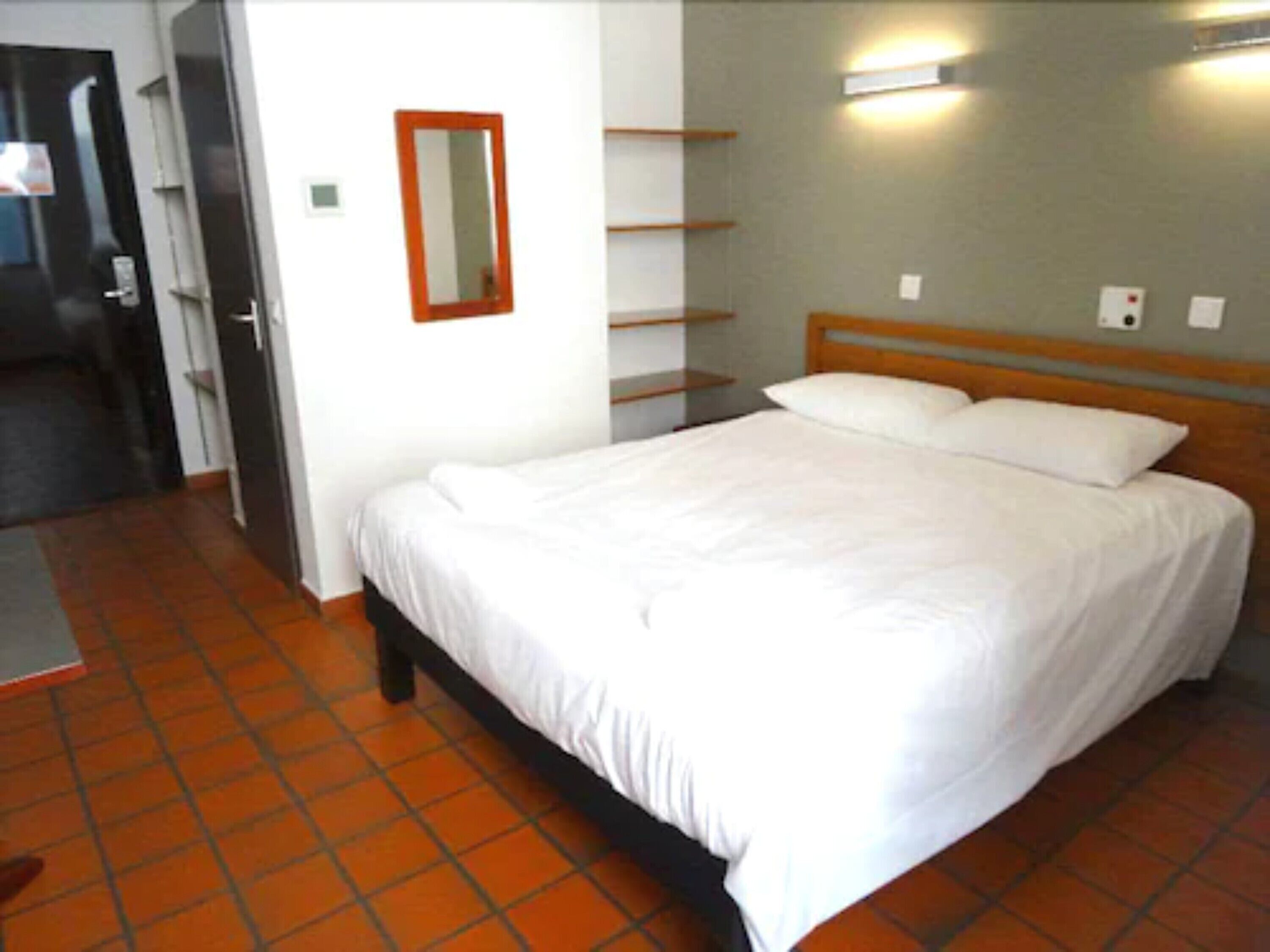 Un dormitorio con cama, cabecera de madera, estante en la pared y una puerta.