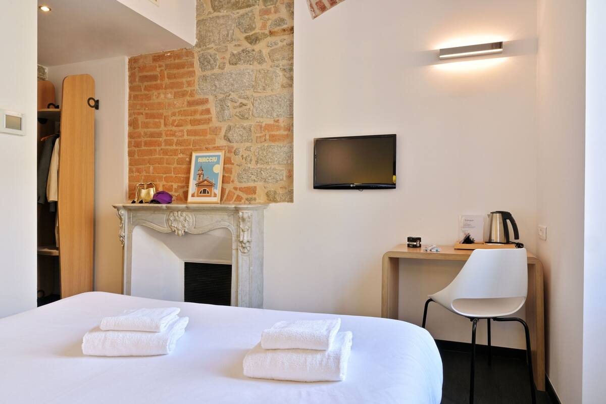 A hotel room with a bed, a TV, a fireplace, and a desk with a chair.