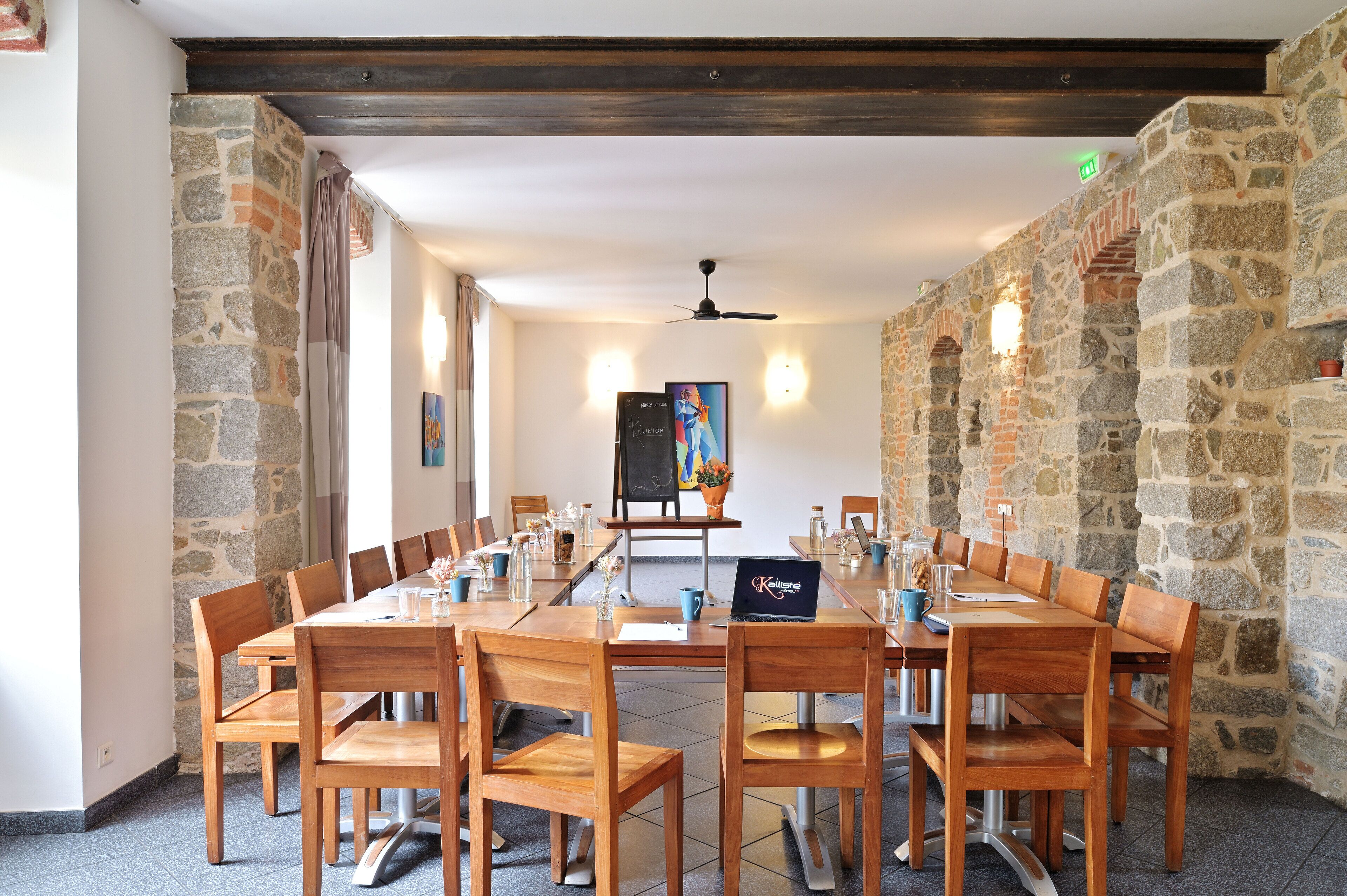 Une salle de conférence avec une longue table en bois, plusieurs chaises, un ordinateur portable et un tableau accroché au mur.