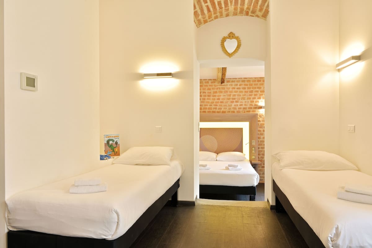 A hotel room with two beds, a brick wall, and a heart-shaped mirror.