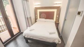 A hotel room with a bed, bedside table, and a view through a sliding door to an outdoor area.