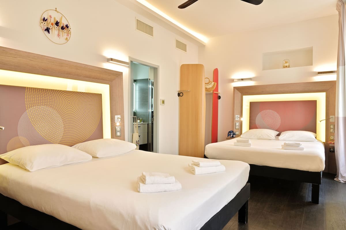 A hotel room with two beds, a wooden headboard, a wall art piece, and a ceiling fan.
