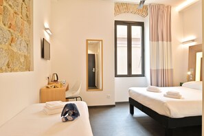 A hotel room with two beds, a stone wall, a flat-screen TV, a wooden side table with a kettle, a chair, and a large window with curtains. - Kallisté Hôtel (Ajaccio)