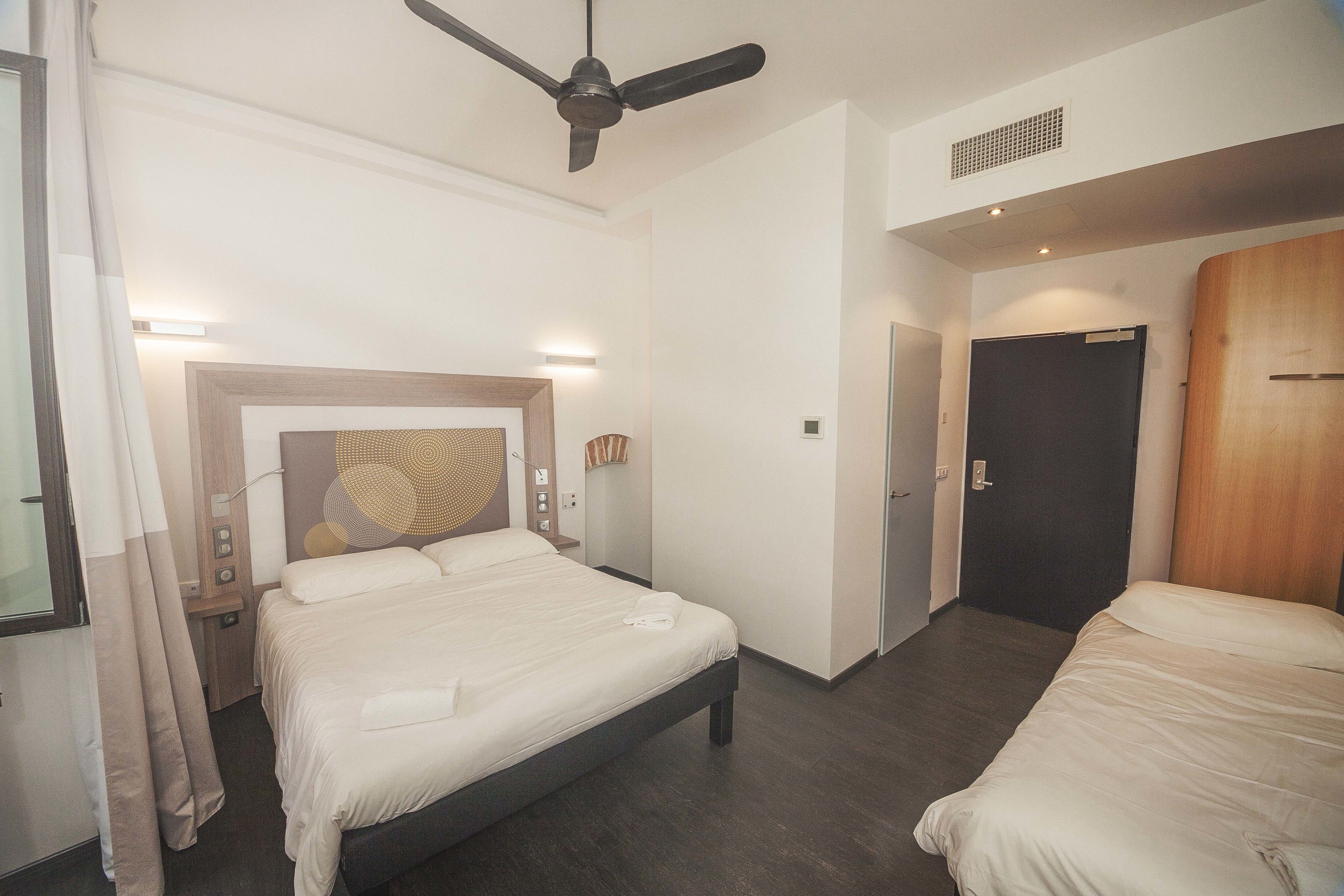 Une chambre d’hôtel avec un lit, un ventilateur de plafond, une table de chevet et une porte.