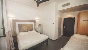 Une chambre d’hôtel avec un lit, un ventilateur de plafond, une table de chevet et une porte.