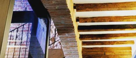 Habitación con vigas de madera a la vista y paredes de ladrillo, un ventanal y vistas a un edificio.