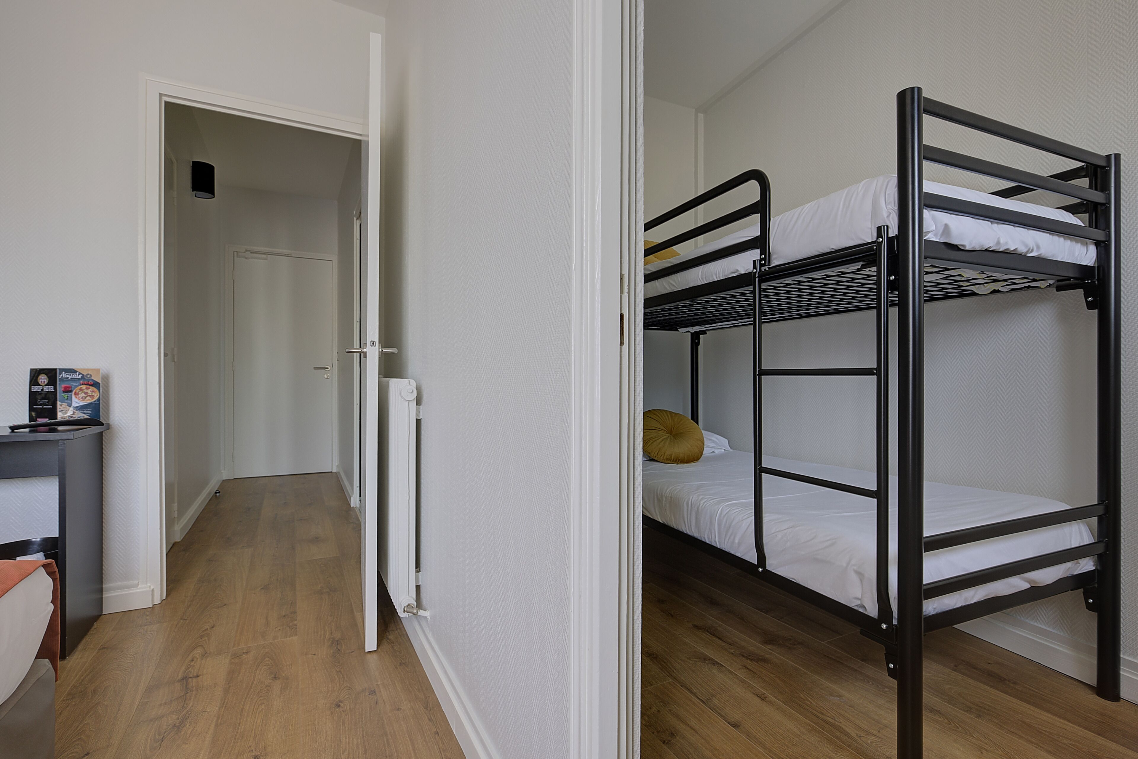 Ein Zimmer mit einem Etagenbett, einem Schreibtisch mit Stuhl und einer Tür zu einem weiteren Raum.