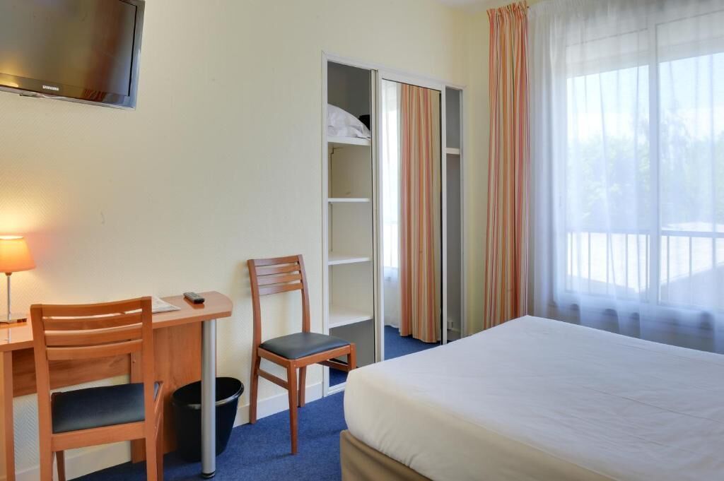 Une chambre d’hôtel comprenant un lit, un bureau avec une chaise, une télévision et une armoire.