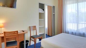 Una habitación de hotel con cama, escritorio con silla, televisor y armario.