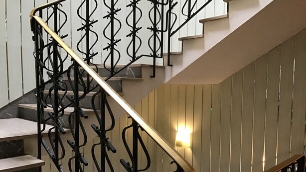 Una escalera con barandillas de metal negro y un pasamanos dorado.