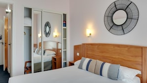 Un dormitorio con cabecera de madera, cama con ropa de cama blanca, espejo circular en la pared y armario con puertas correderas.