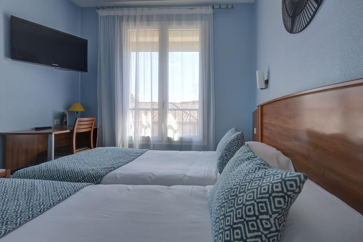 Ein Hotelzimmer mit zwei Betten, einem Schreibtisch, einem Sessel, einem Fernseher und einem Fenster mit Vorhängen.