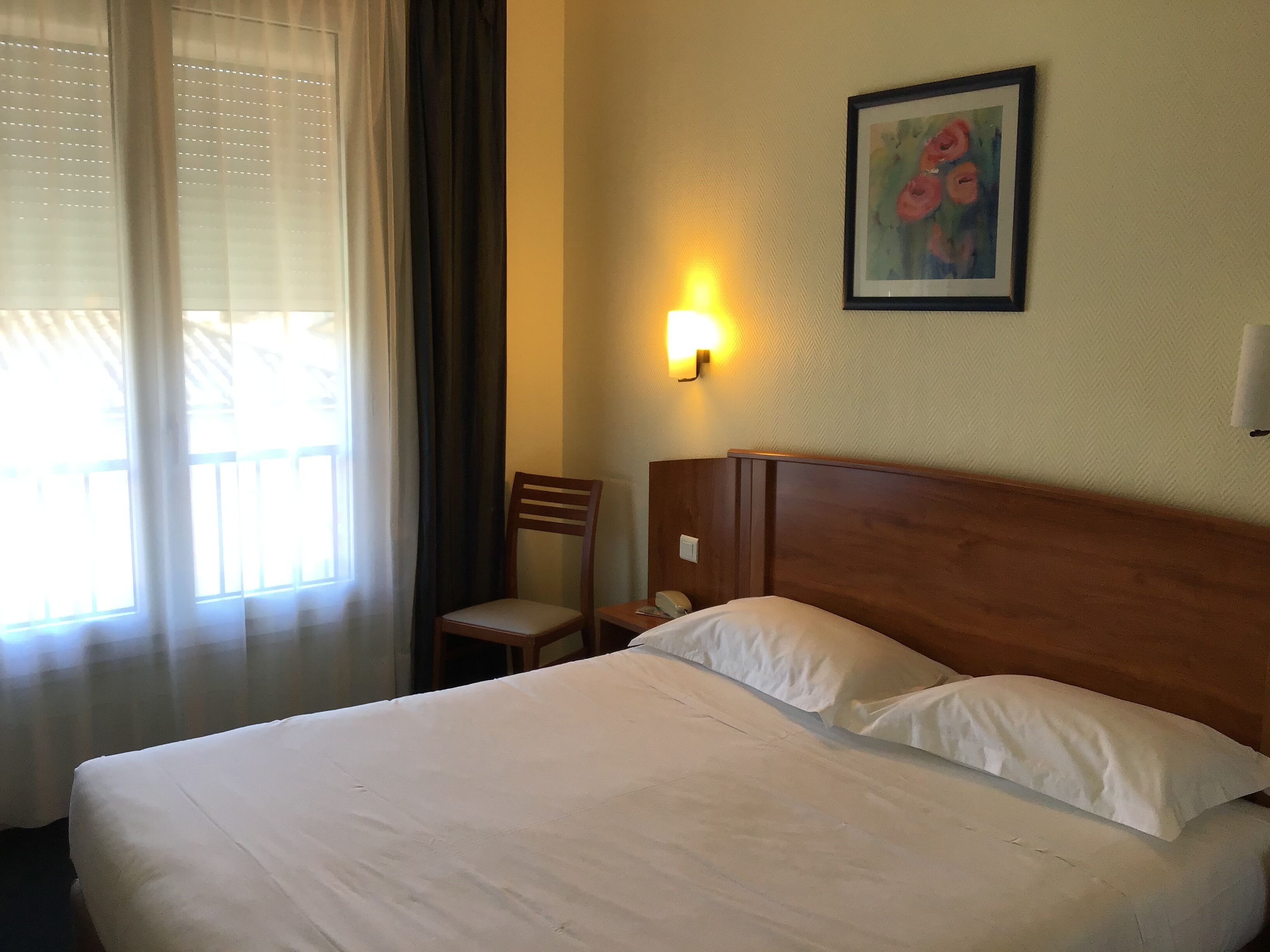 Une chambre d’hôtel avec un grand lit, une chaise, une table de chevet avec une lampe et un tableau au mur.