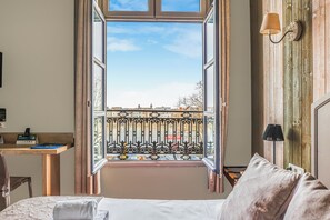 A hotel room with a large window, a desk, a bed, and a wall-mounted lamp. - Logis Hotel Restaurant Cristal (Saumur)