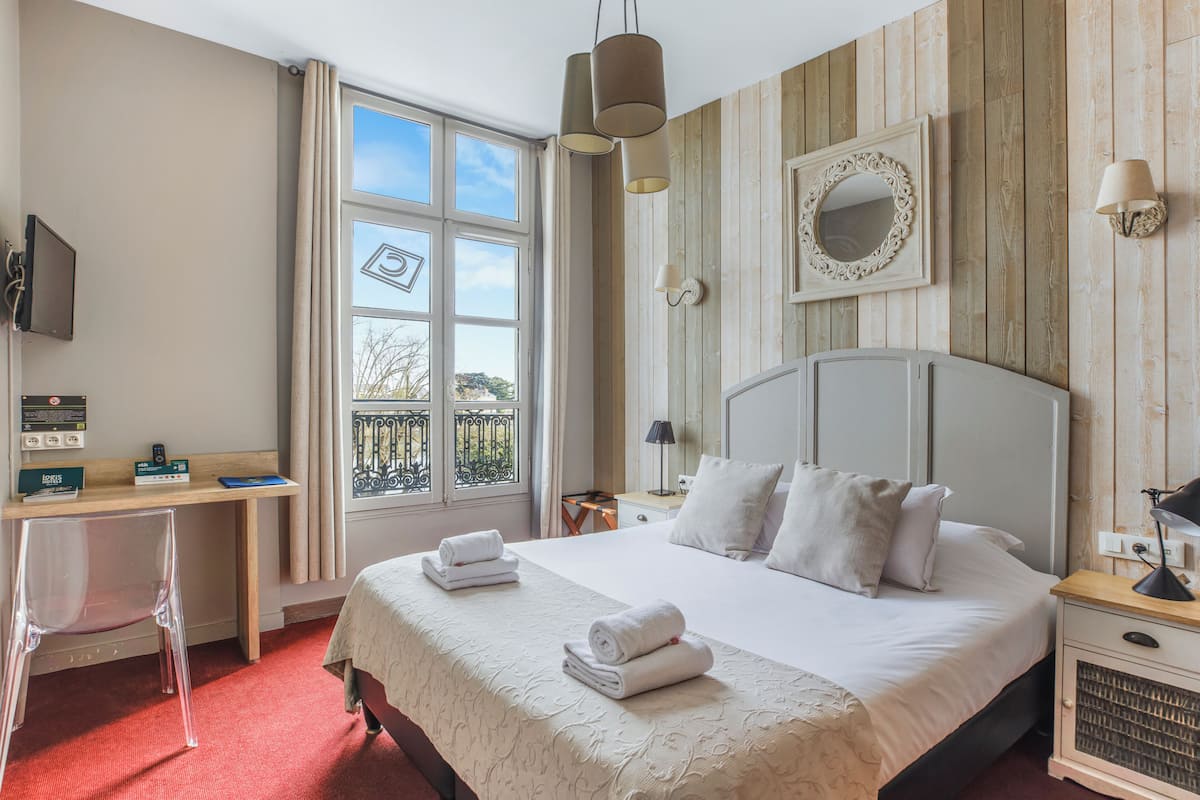 A hotel room with a bed, a desk, a chair, a TV, a window, and a view of the outdoors.