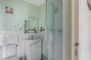 A bathroom with a toilet, sink, mirror, and glass shower enclosure. - Logis Hotel Restaurant Cristal (Saumur)