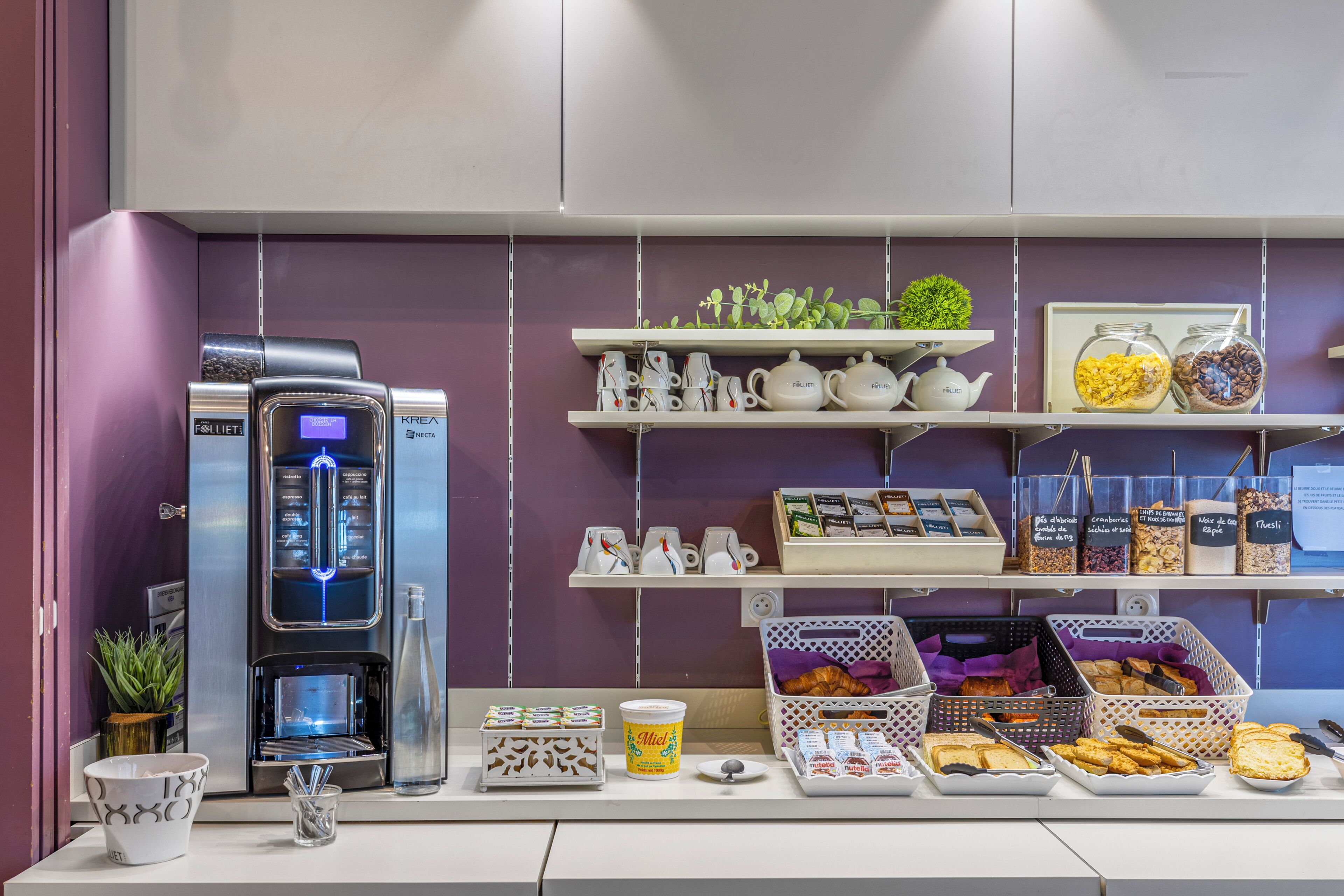 A breakfast bar with coffee machines, tea pots, and various food items.