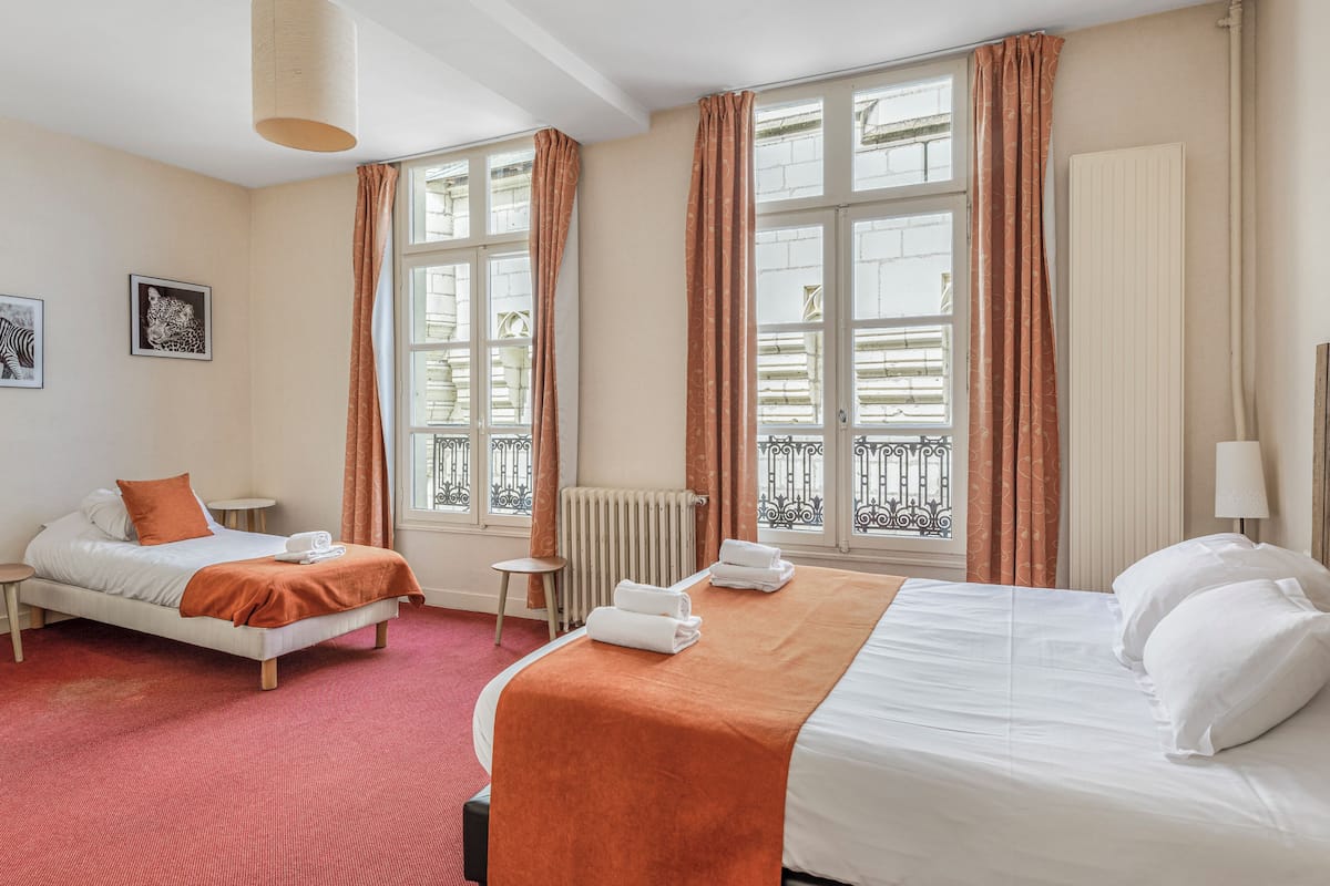 A hotel room with two beds, a radiator, a small table, and a window with curtains.