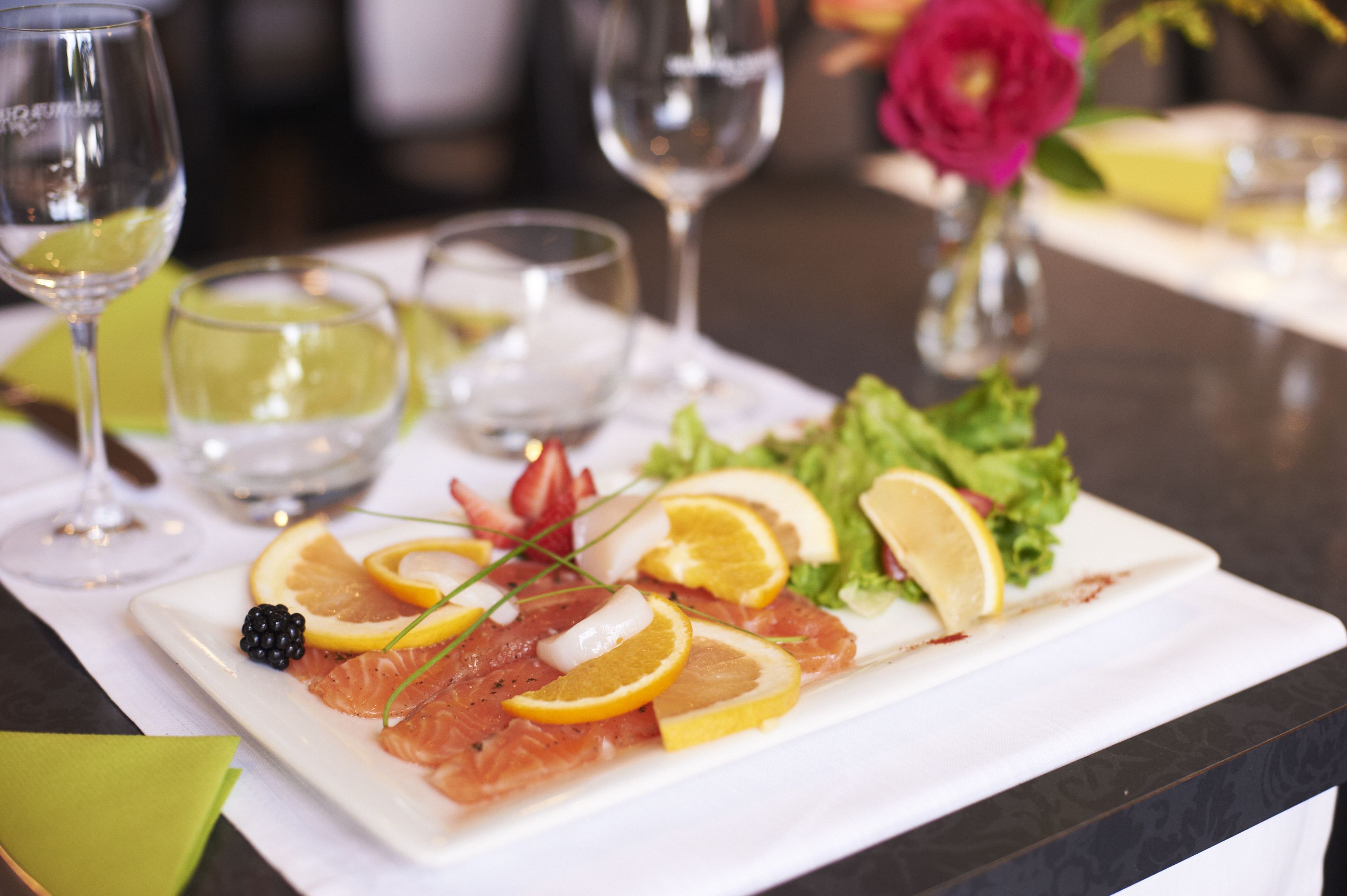 A plate of food with salmon, lemon slices, and blackberries, accompanied by a glass of white wine.