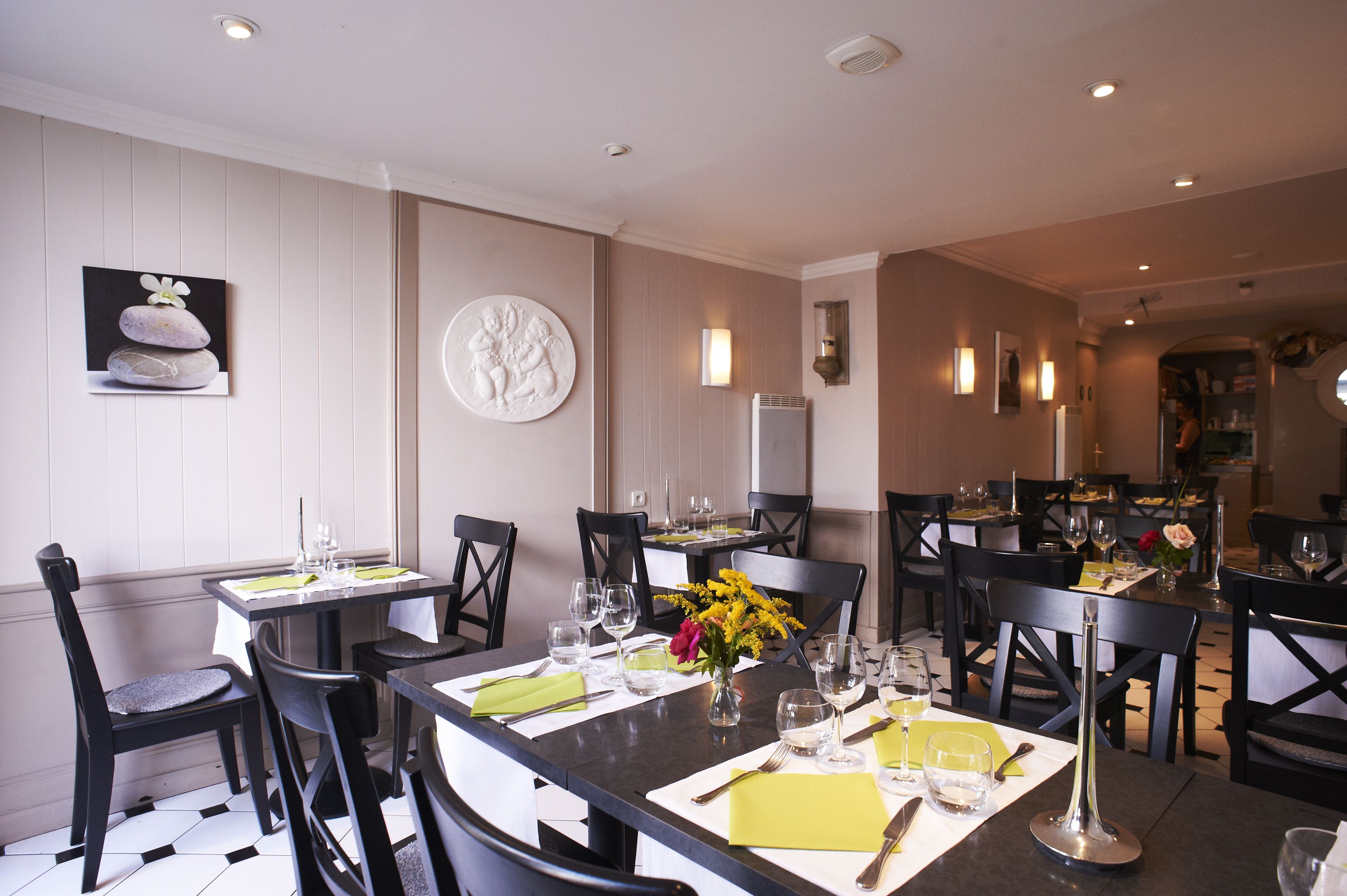 A dining area with multiple tables set for guests, featuring a modern design with black chairs and white tablecloths.