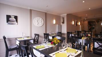 A dining area with multiple tables set for guests, featuring a modern design with black chairs and white tablecloths.