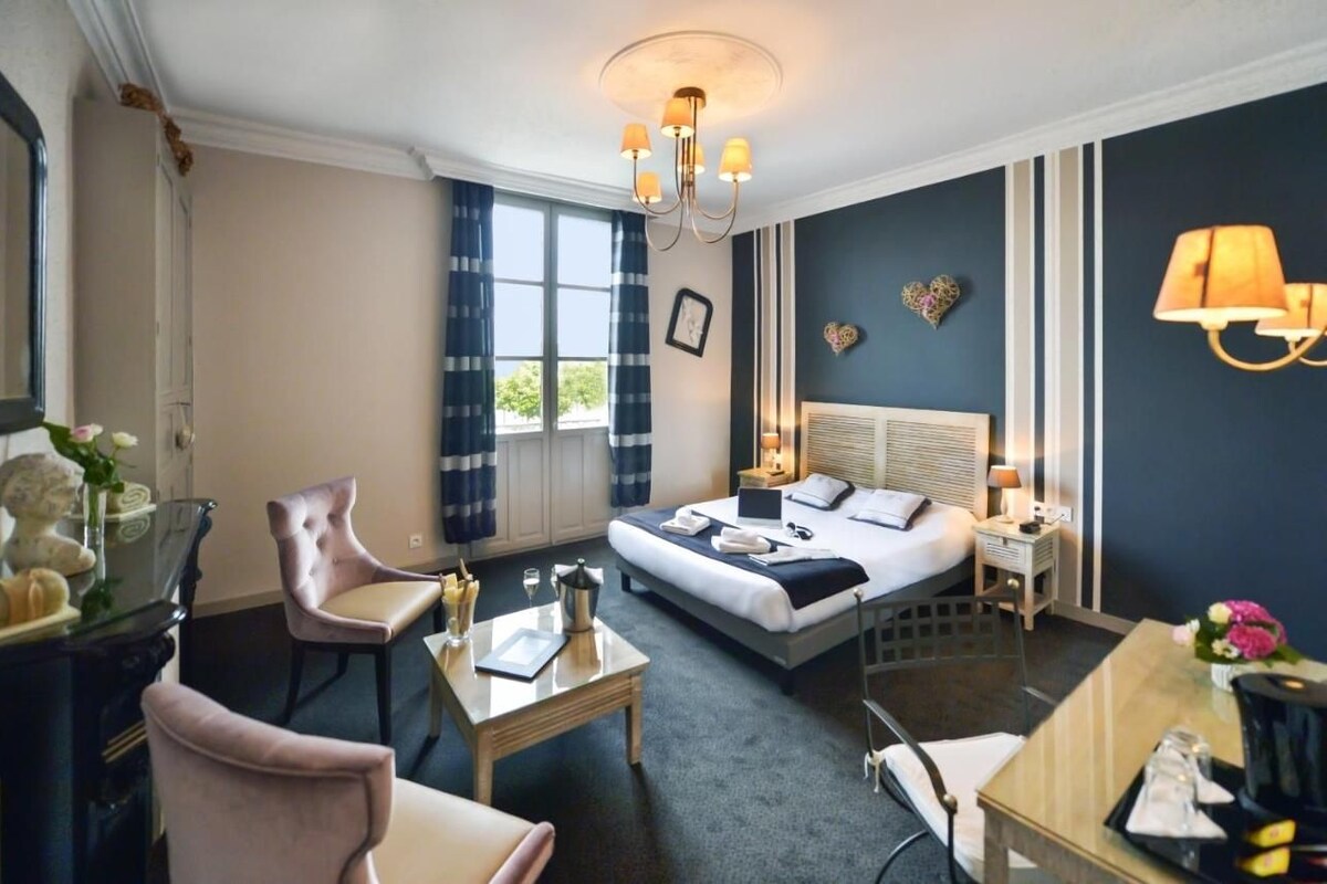 Habitación de hotel con cama, mesita de noche, lámpara, silla y vistas al exterior.