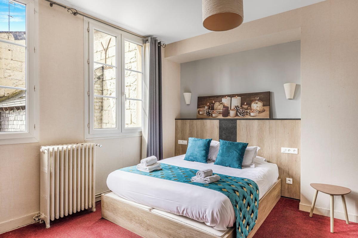 A bedroom with a bed, a radiator, a window, and a small table.
