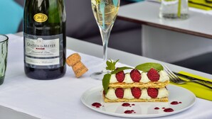 Una botella de vino Gratin & Meyer, una copa de vino blanco y un postre con frambuesas y hojas de menta en un plato.