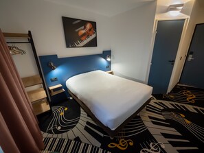 A hotel room with a bed, a headboard with a violin painting, a nightstand, a lamp, and a door. - Welcomotel Beauvais Aéroport (Beauvais)