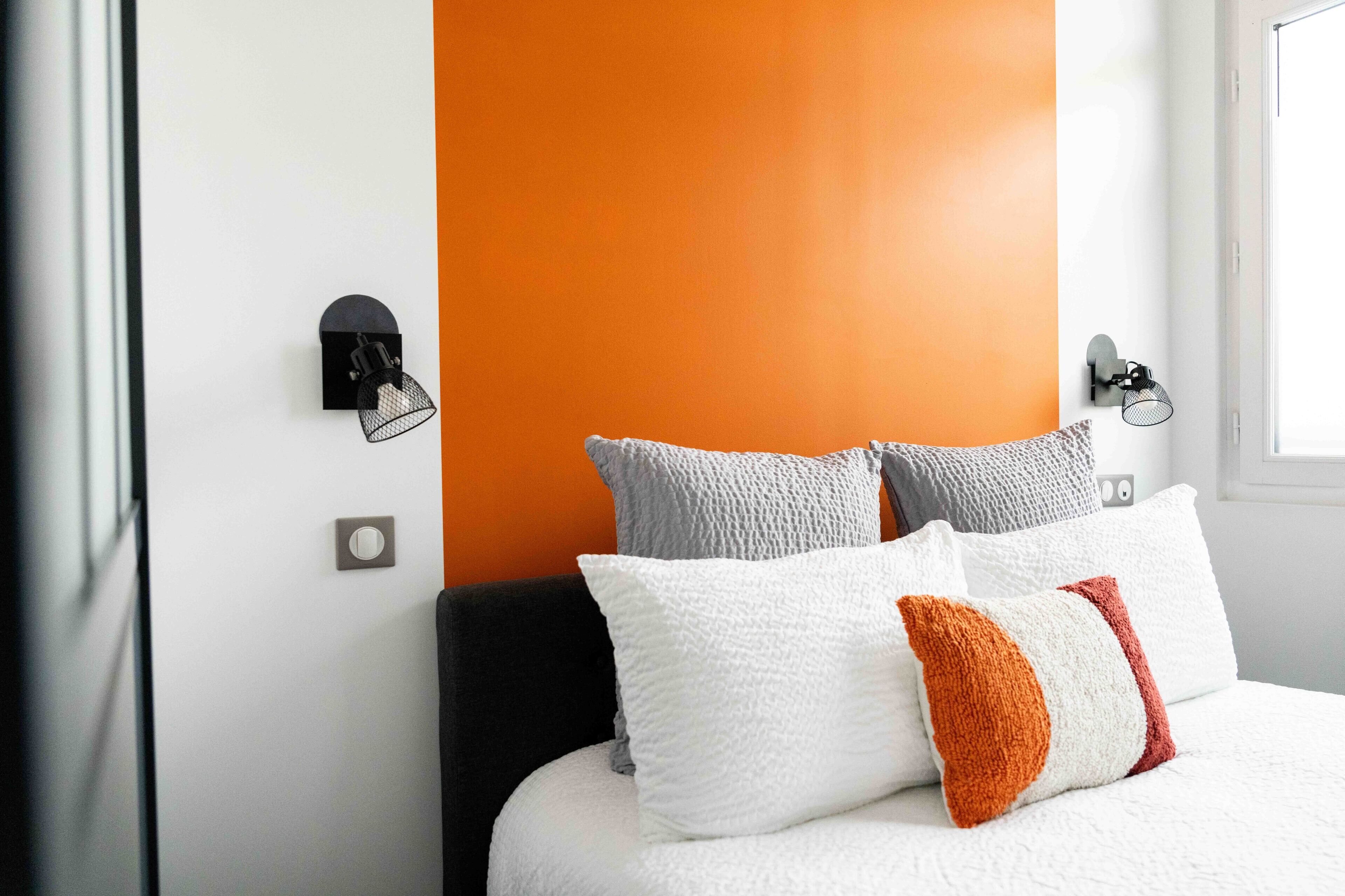 A bedroom with a bed, two wall-mounted lights, and a window.