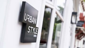 Ein schwarzes Schild mit weißer Schrift, das "URBAN STYLE HOTEL" zeigt, an einer weißen Wand angebracht.