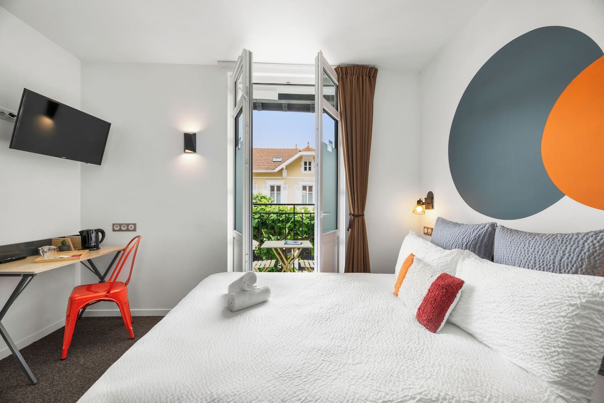 Hotellihuone, jossa on sänky, työpöytä tuolilla, televisio ja näkymä ulos.