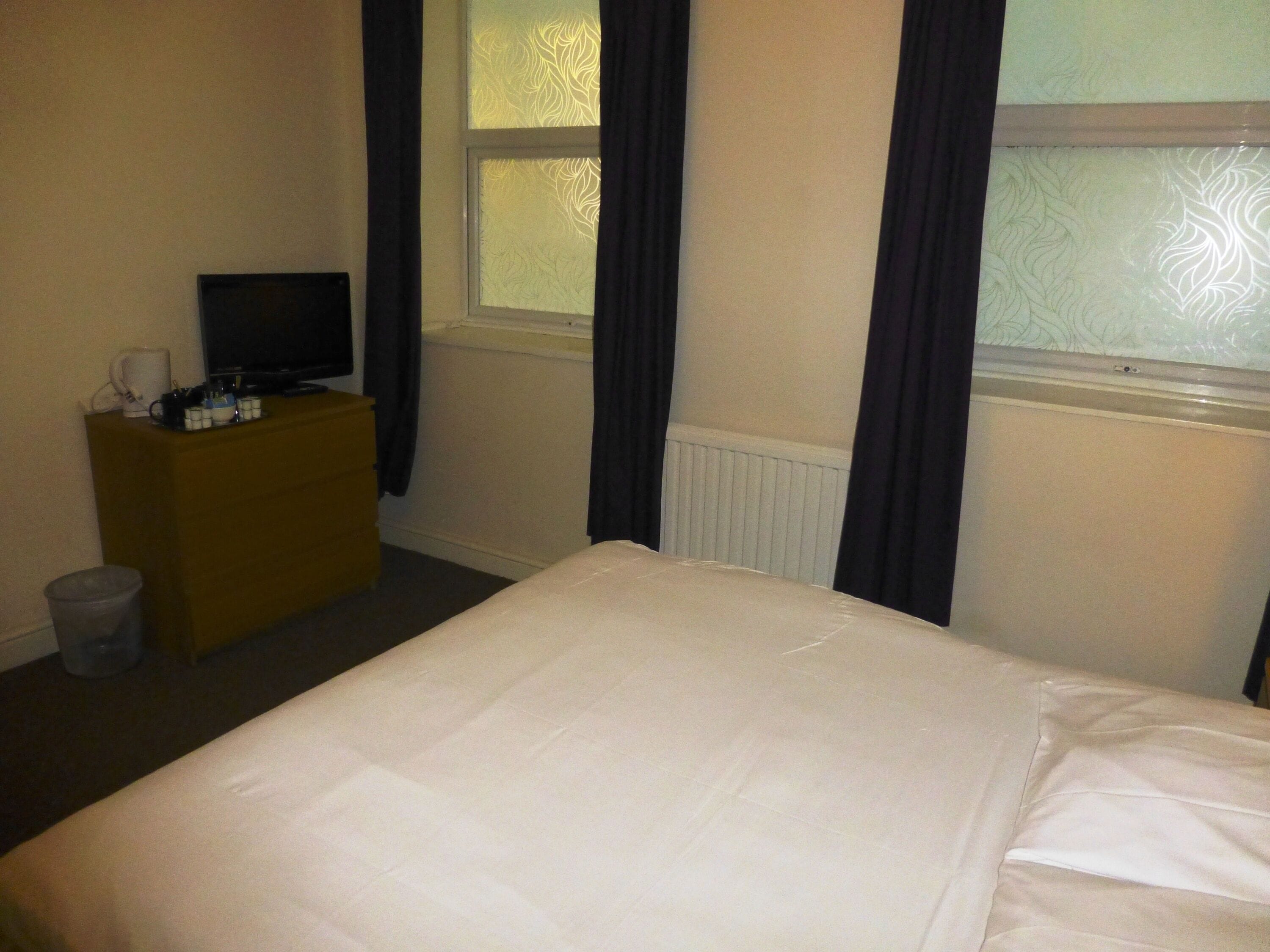 A hotel room with a bed, a small wooden dresser, a television, and a window with curtains.