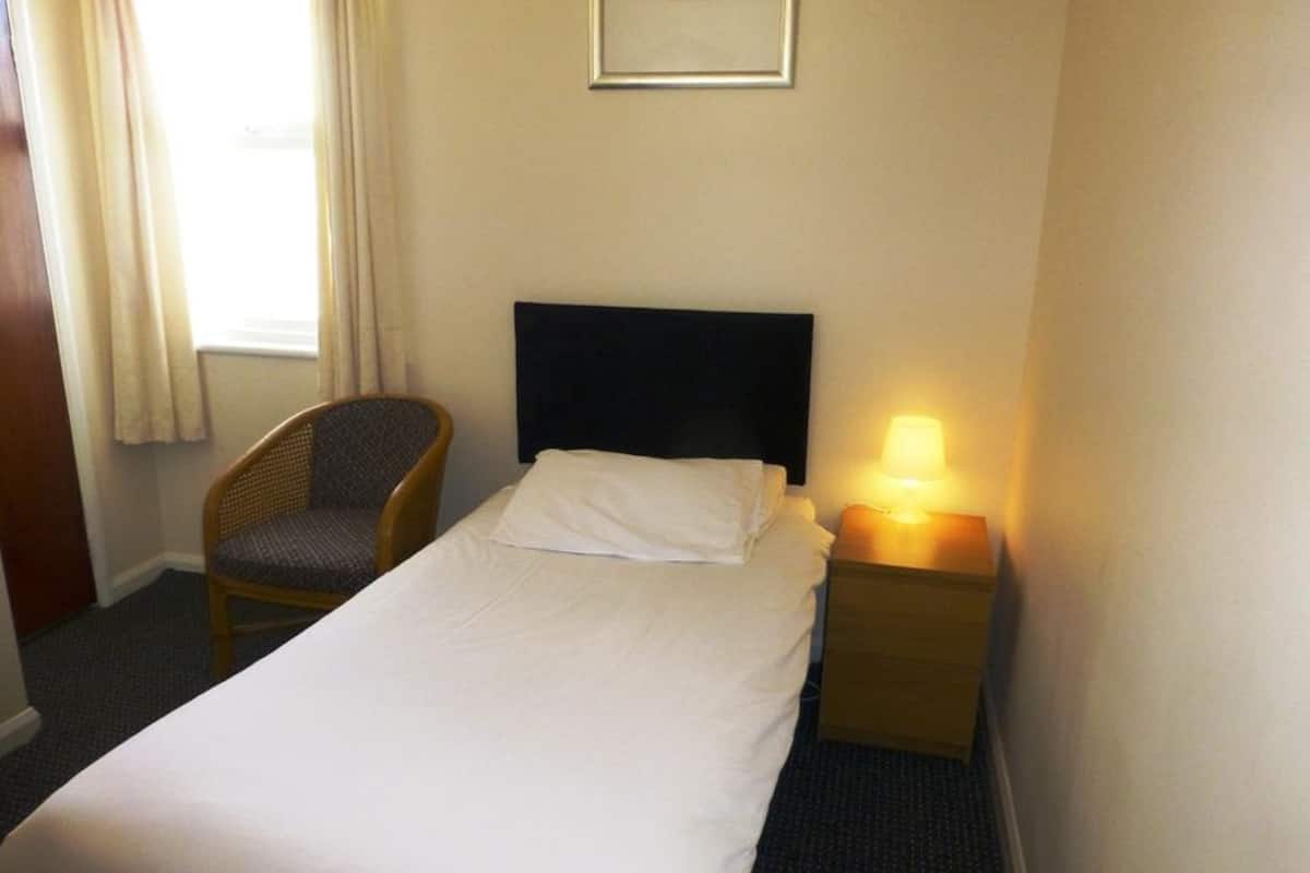 A hotel room with a bed, a chair, a nightstand with a lamp, and a framed picture on the wall.