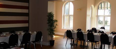 A dining area with tables set for a meal, large windows, and a flag on the wall.