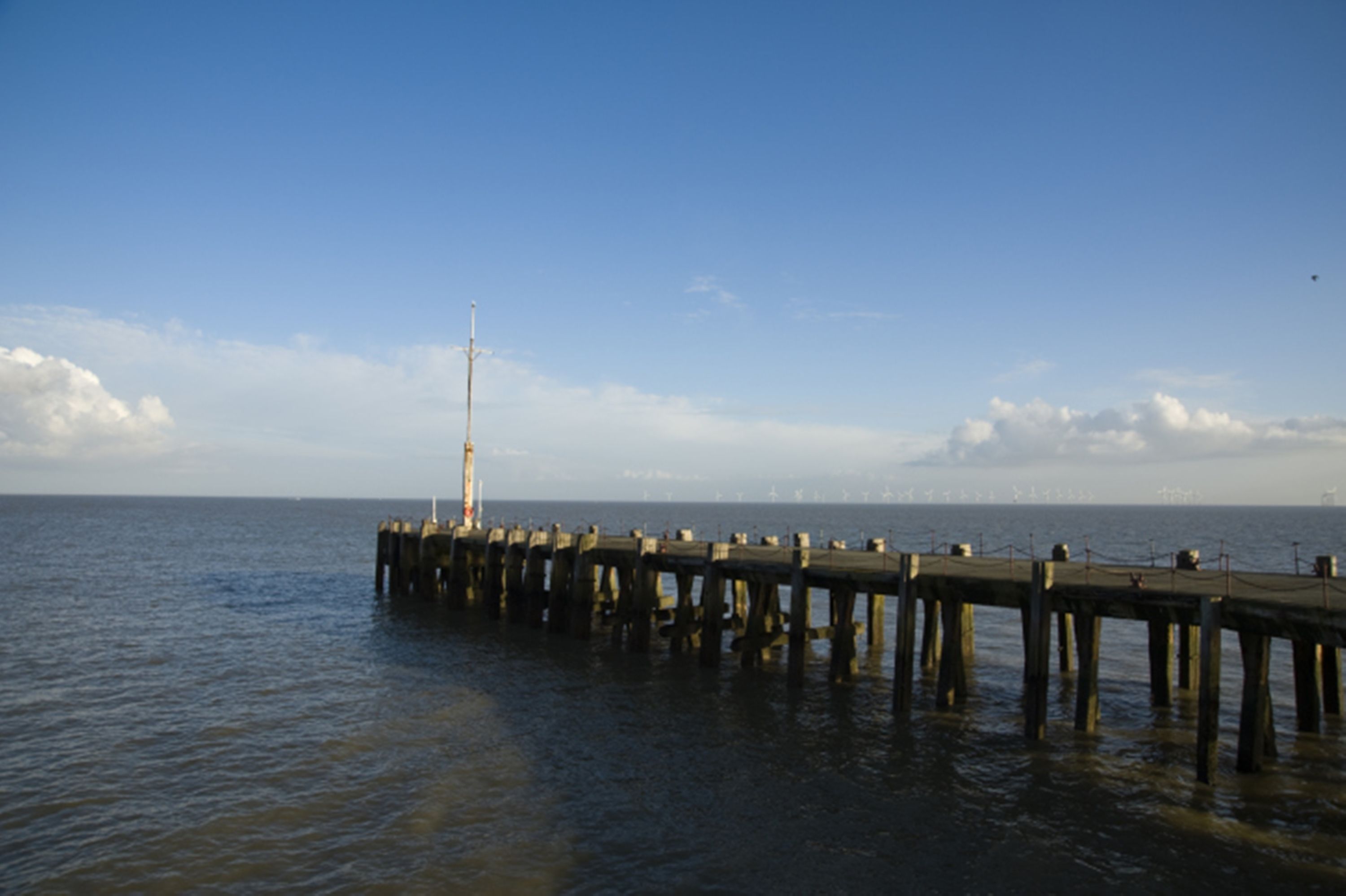 A pier extending into calm water with a clear sky above.