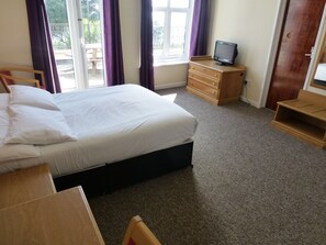 A hotel room with a bed, a wooden dresser, a television on a stand, and a window with curtains. - Esplanade Hotel - Clacton On Sea (Beachfront Hotel) by OYO (Clacton-on-Sea)
