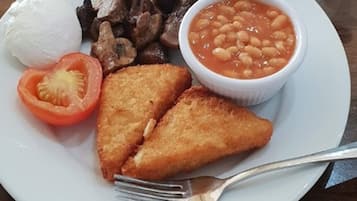 Un plato con un huevo cocido, champiñones fritos, frijoles horneados, una rodaja de tomate y dos preparaciones fritas.