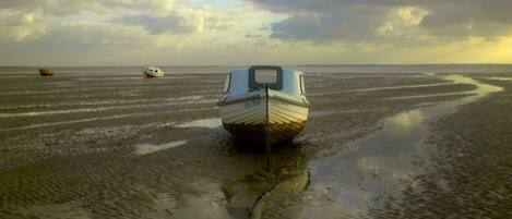 A boat on a wet beach with another boat in the distance.
