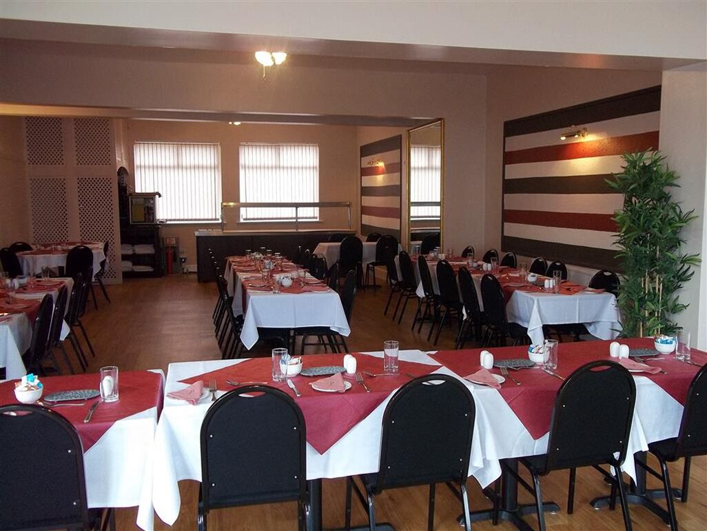 A dining area with multiple tables set for meals, chairs, and a large mirror on the wall.