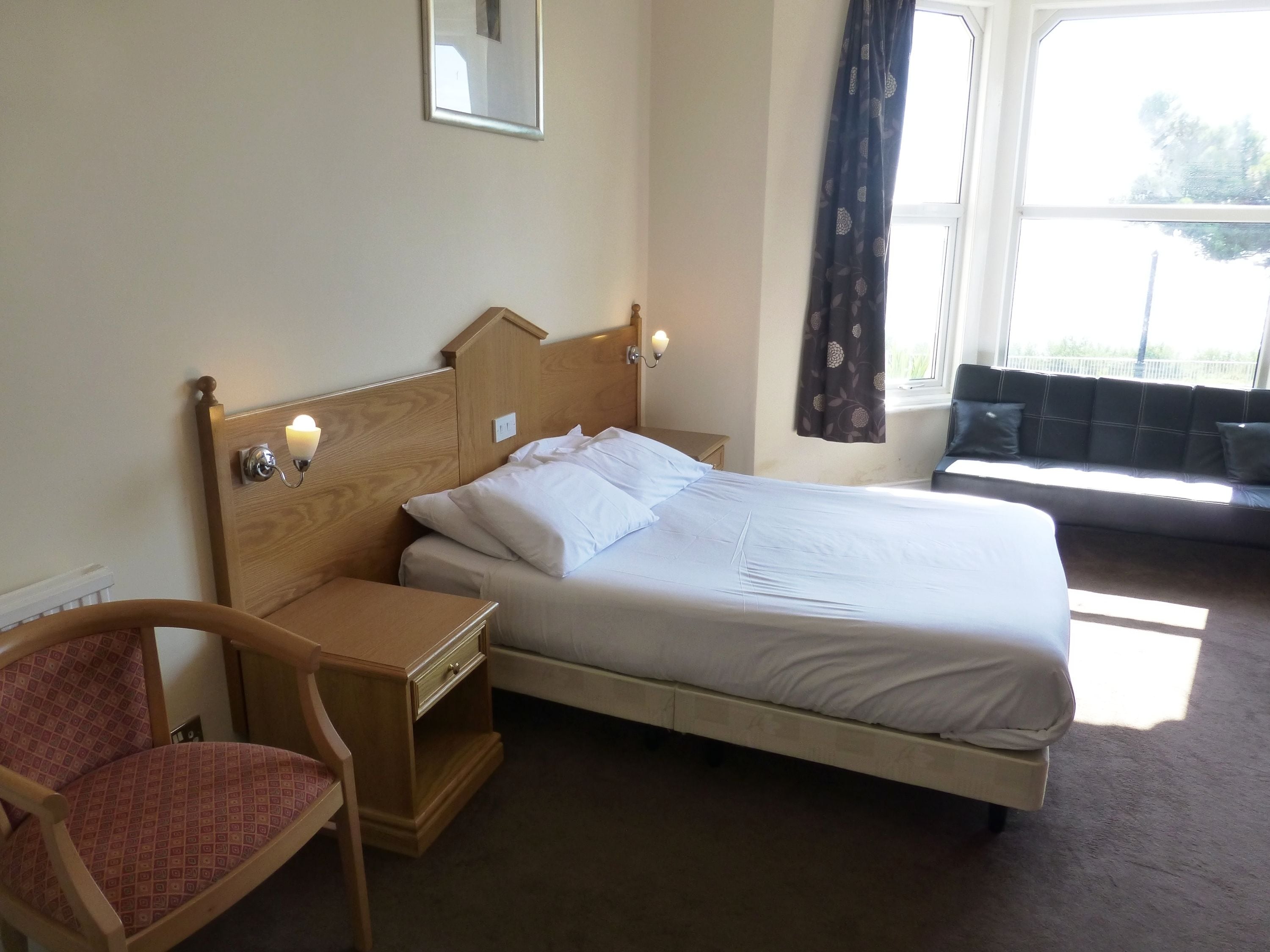 Ein Hotelzimmer mit Bett, Nachttisch, Stuhl und einem Fenster mit Vorhängen.